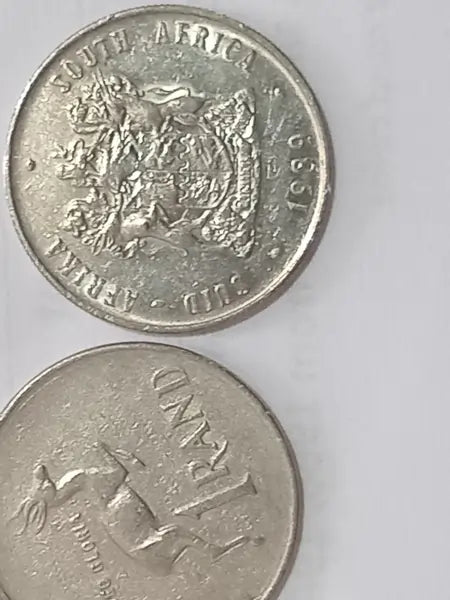 Two 1989 R1 coins from South Africa. Obverse: Coat of arms of South Africa
Reverse: Springbok, denomination below, date above. Displayed on a white background