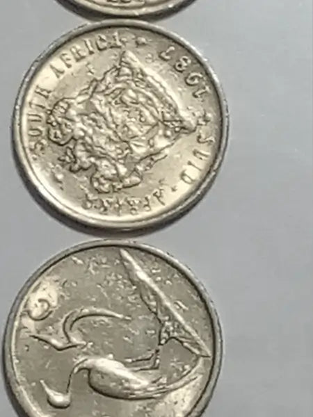 Two 1987 5 cent coins from South Africa on a gray background