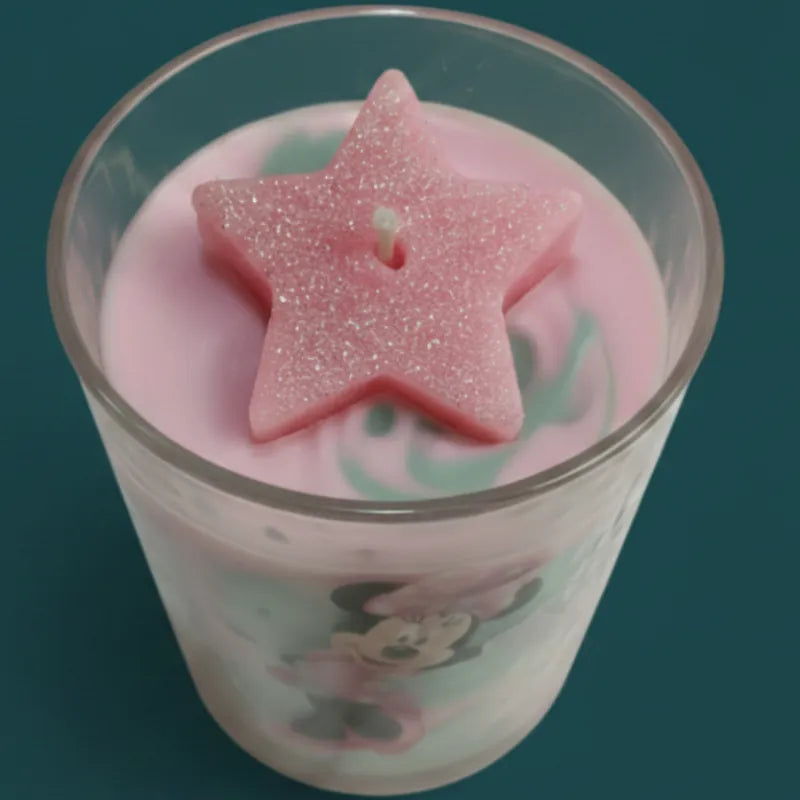 Minnie Mouse candle in Glass with pink and green liquid and a star-shaped pink candy on a dark background.Aerial view