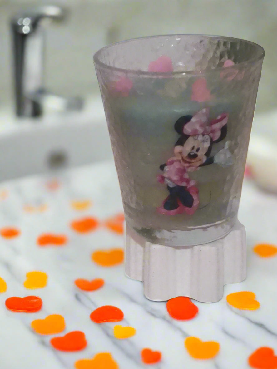 Glass with Minnie Mouse design on a white surface with pink petals