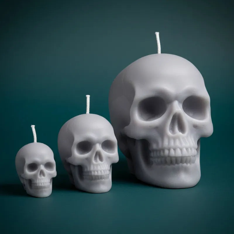 Three skull-shaped candles of different sizes on a dark green background