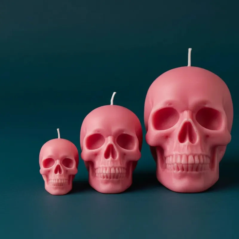 Three pink skull-shaped candles of different sizes on a dark blue background