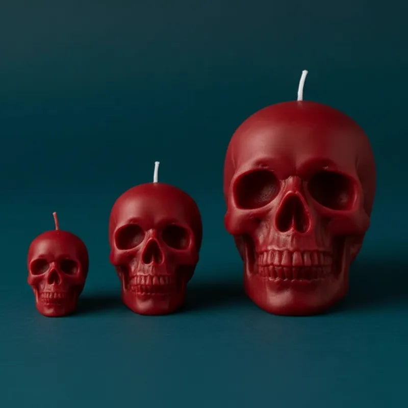 Three red skull-shaped candles of different sizes on a dark blue background